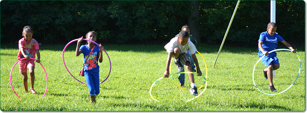 Four children playing with hula hoops outdoors in a sports field. 