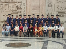 A group photo of all the graduates, faculty, and staff dressed in graduation caps and gowns, standing in three neat lines. 