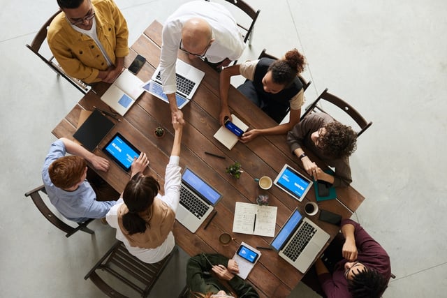 a group of people sitting around a table with laptops