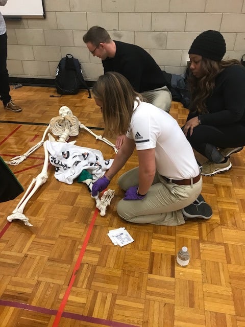 Three participants work on a medical skeleton model on a gymnasium floor