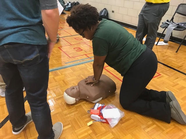 a student person in a green shirt is practicing CPR on a dummy on the floor