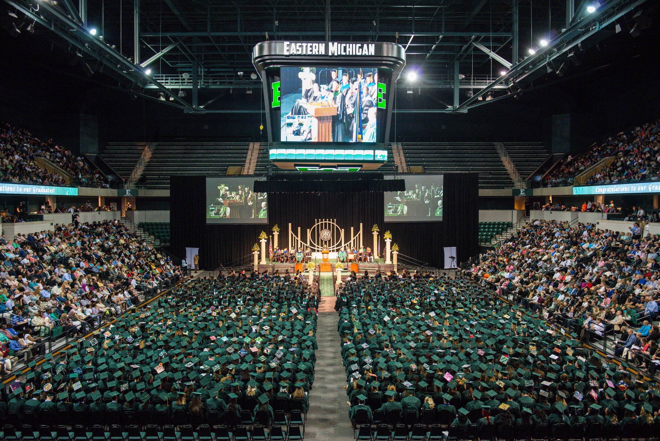 a large auditorium filled with people in EMU graduation gowns.