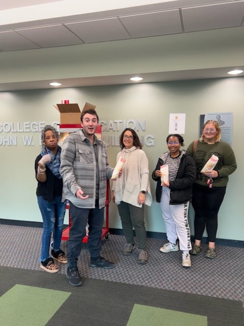 A group of EMU students and staff pose for a photo in front of the College of Education sign 