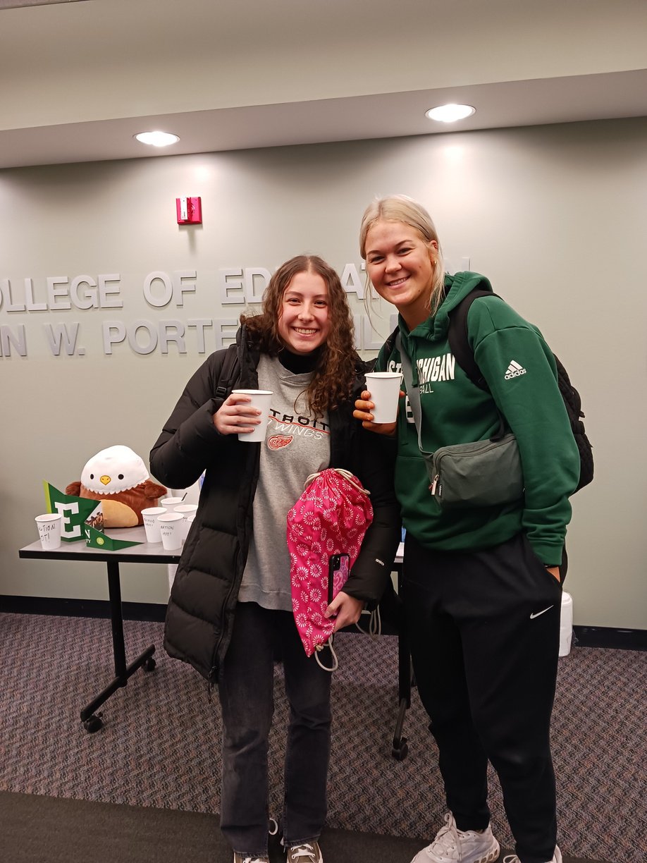 two students standing in front of a table holding hot cocoa cups