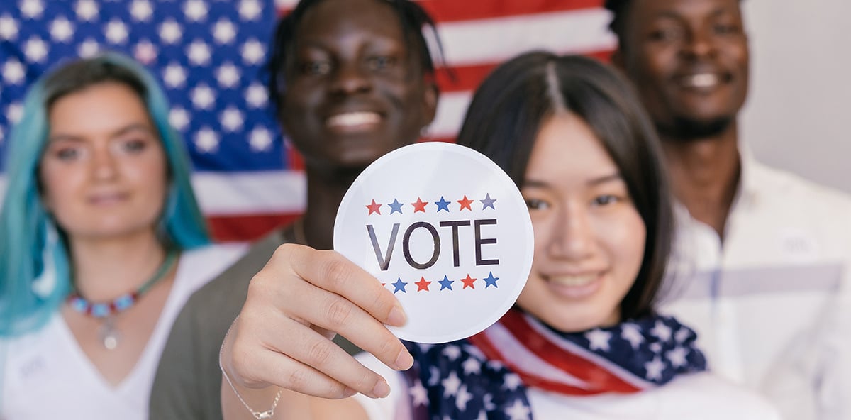 a group of people holding up a vote sign in front of an American flag.