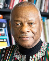 an individual wearing a colorful shirt standing in front of a bookshelf.