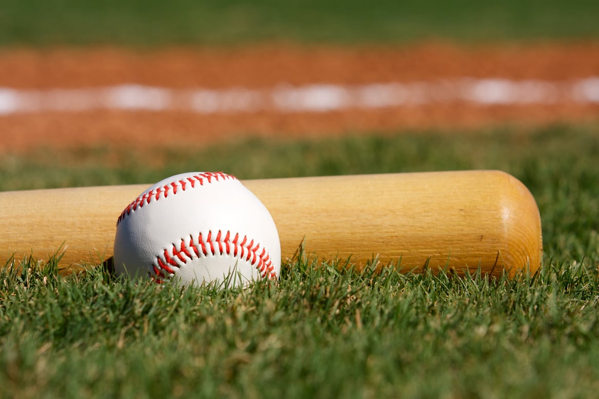 a baseball and bat sit on the grass in front of a baseball field