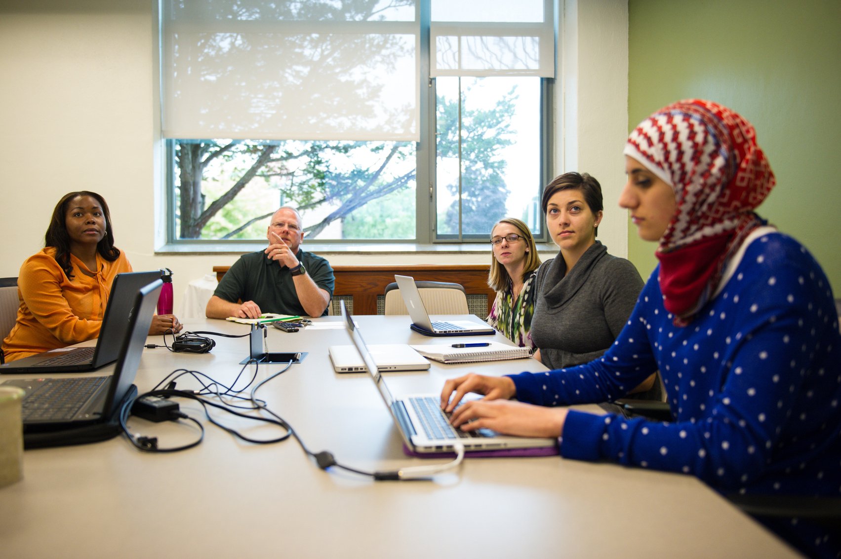 a group of people sitting around a table with laptops