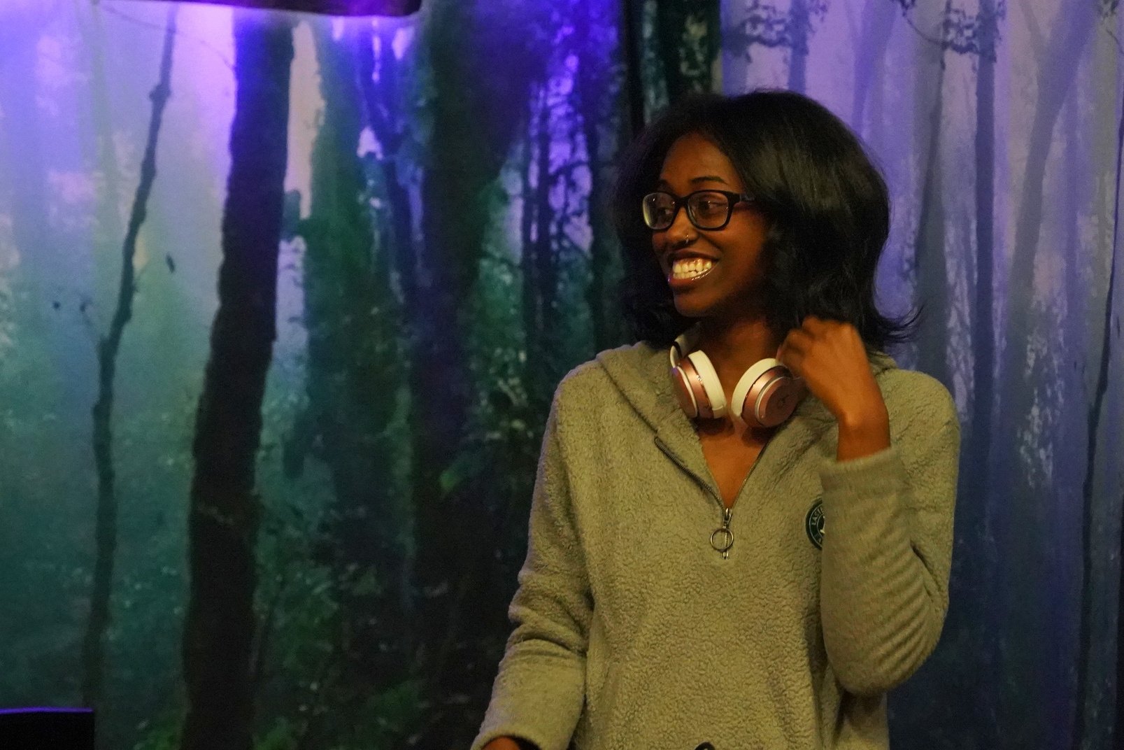 a person wearing headphones smiles while standing in front of a forest background