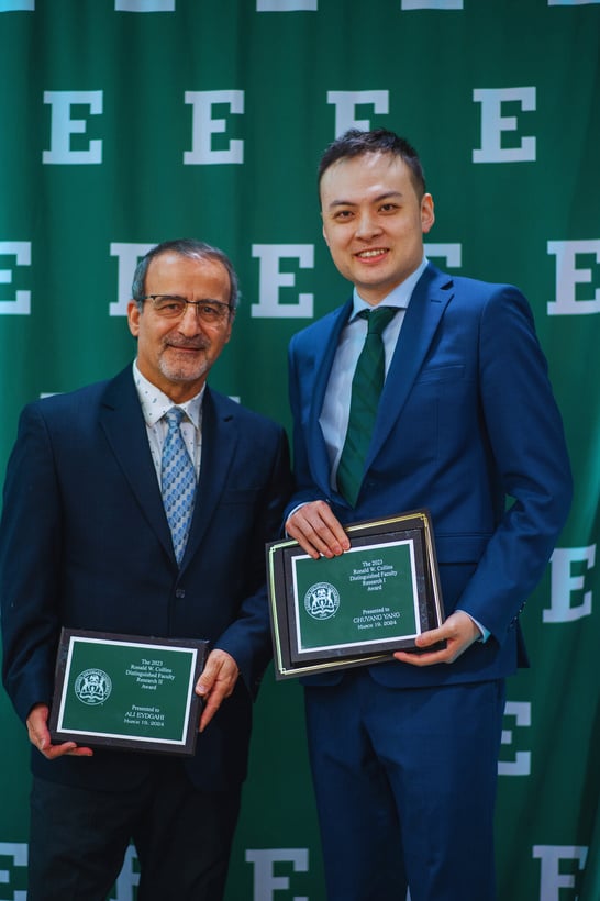 two people in suits holding awards in front of a green wall