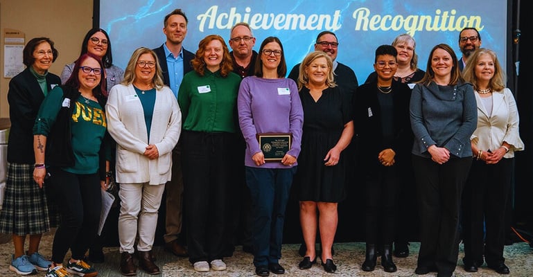 a group of people standing in front of a screen with a banner that says achievement recognition