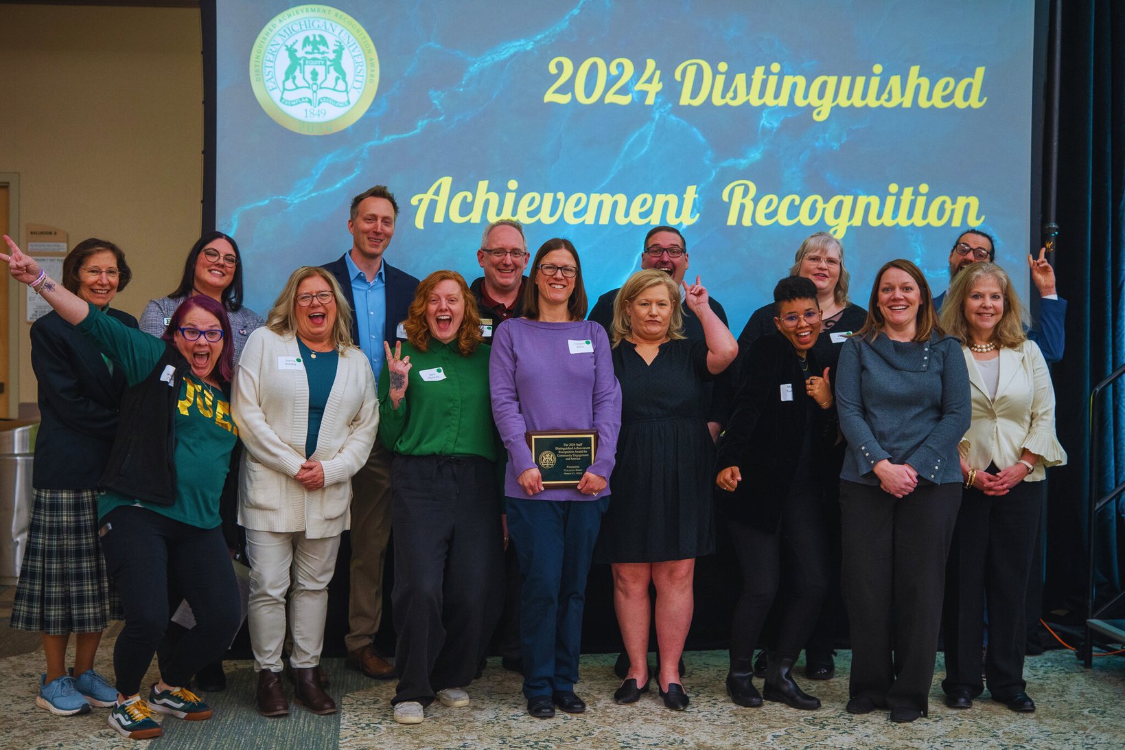 a group of people posing with silly faces for a photo in front of a screen that says achievement recognition