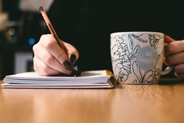 a hand writing in a notebook with a cup of coffee