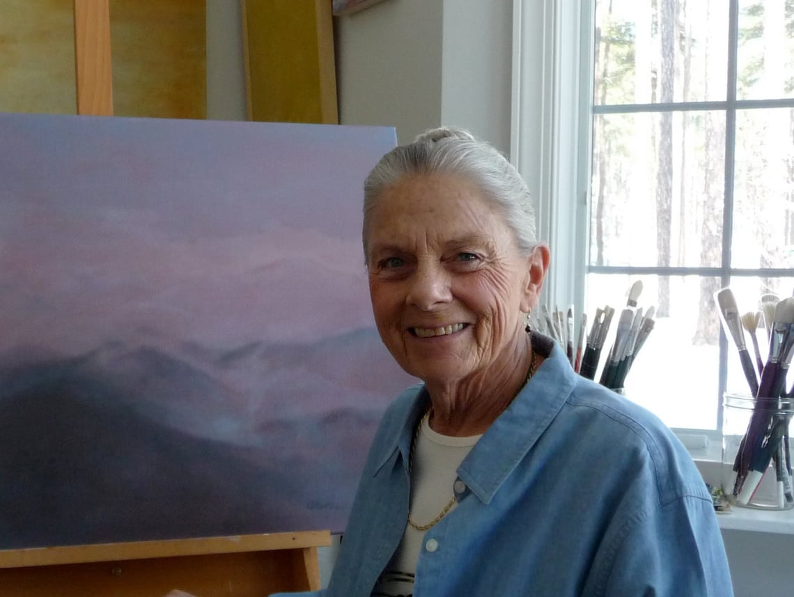 Annette Martin poses in front of a mountainous landscape painting