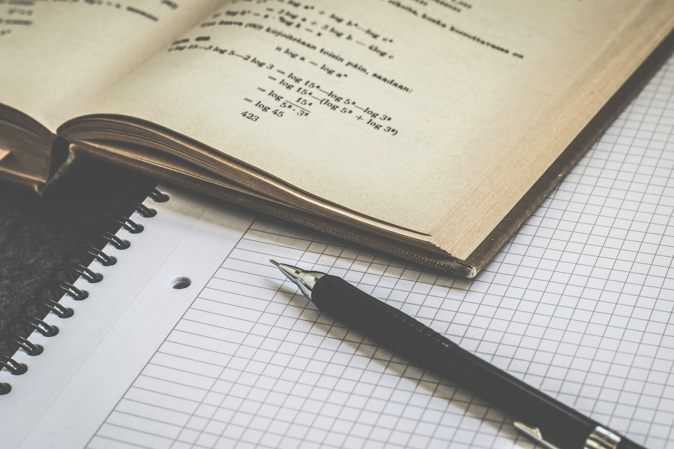 an open notebook showing mathematical formulae with a pen on top of it