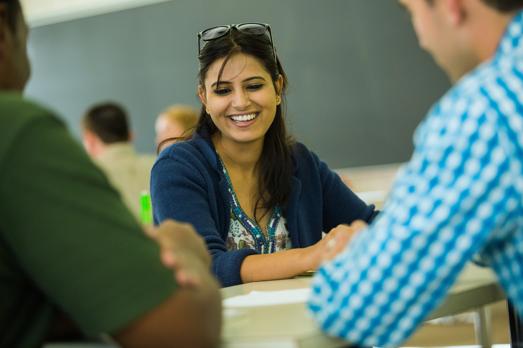 a smiling person sitting at a table in front of a group of people