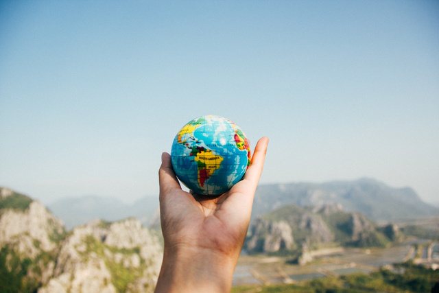 A hand holding a small world globe on top of a mountain