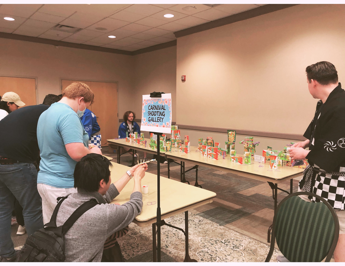 a group of people attempt a bamboo rubber-band shooting gallery