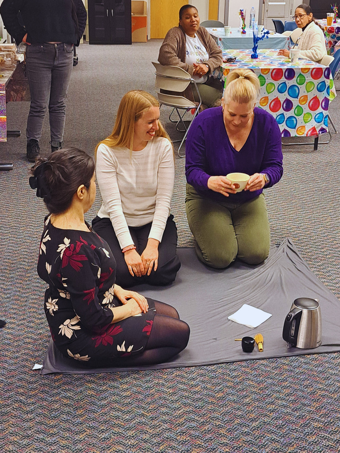 Three people kneel on a mat in a conference room. 