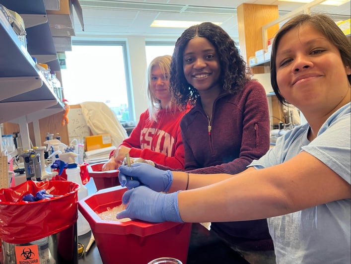 three young students in lab coats and gloves are smiling at the camera