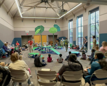 A venue hall with a circle of attendees surrounding a stage decorated with green umbrellas.