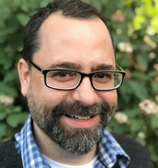 Patrick Flores-Scott pictured with glasses and a beard smiles for the camera