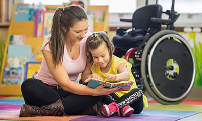 a person reading to a little person with a wheelchair in the background