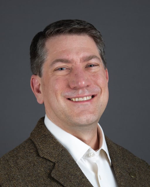 Dr. John McCurdy pictured in a brown jacket and white shirt smiling