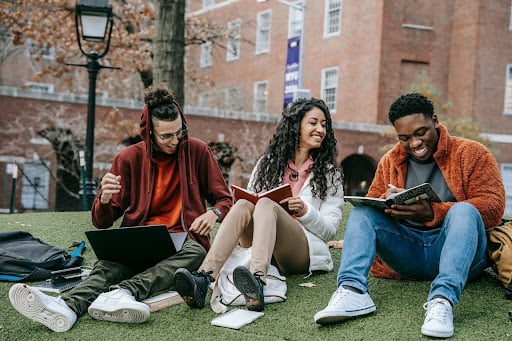 a group of students sitting on the grass in front of a building