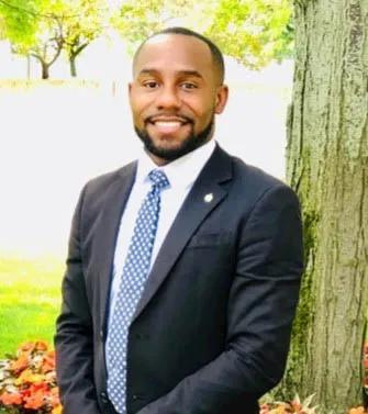 Anthony Webster pictured in a suit and tie standing in front of a tree