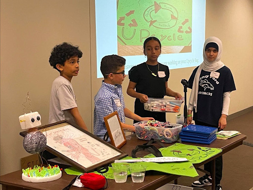 a group of kids standing around a table with some Up Cycle presentation items on it