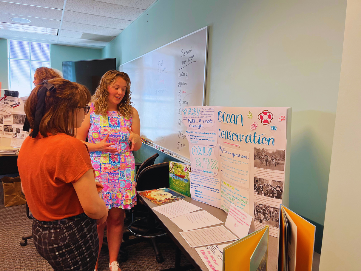 two people standing in front of a table with a poster on it