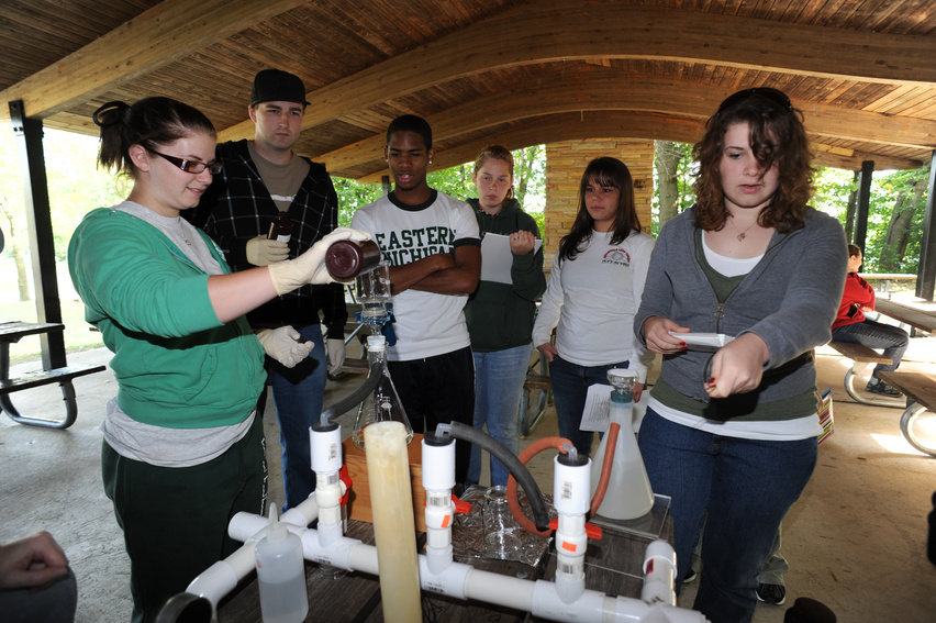 a group of people standing around a science experiment in an outdoor space