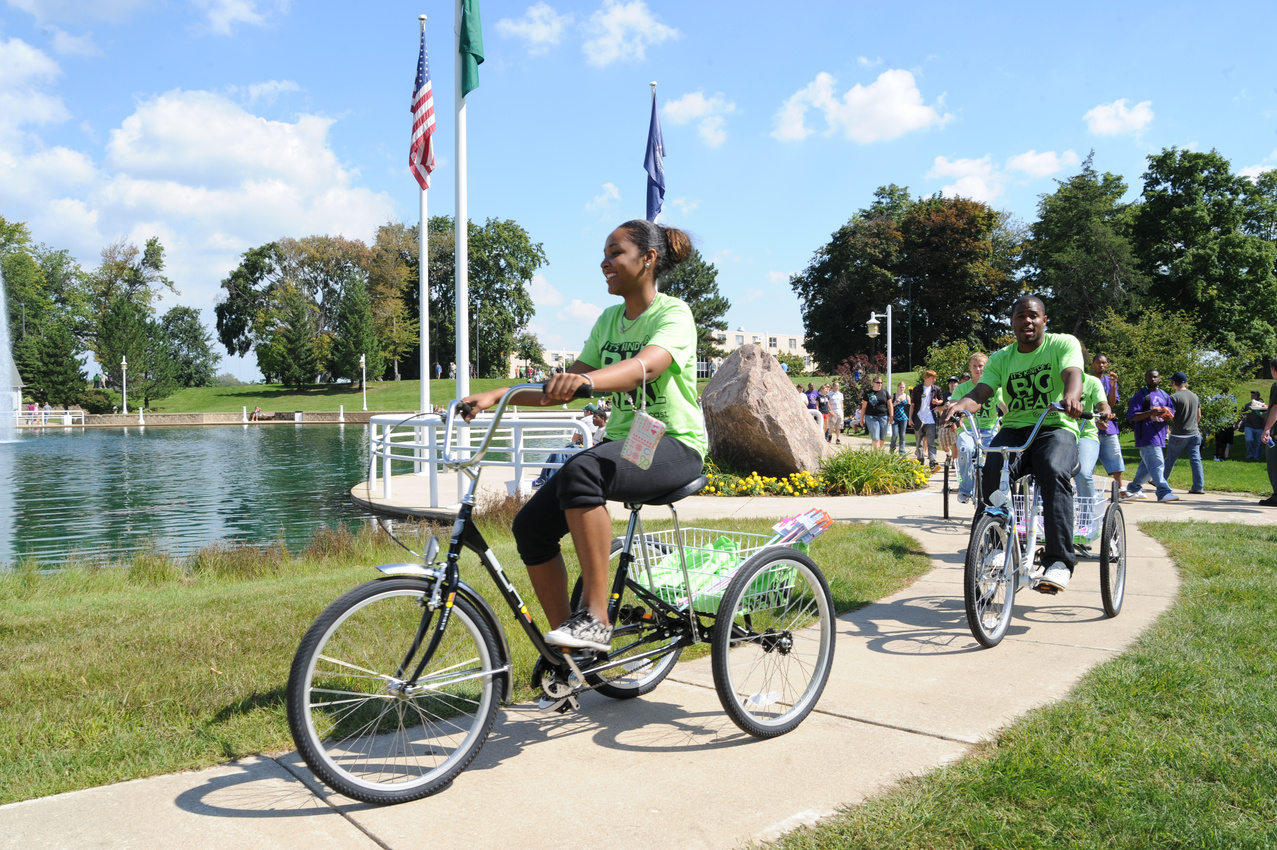 a student in a green shirt is riding a bike near a lake