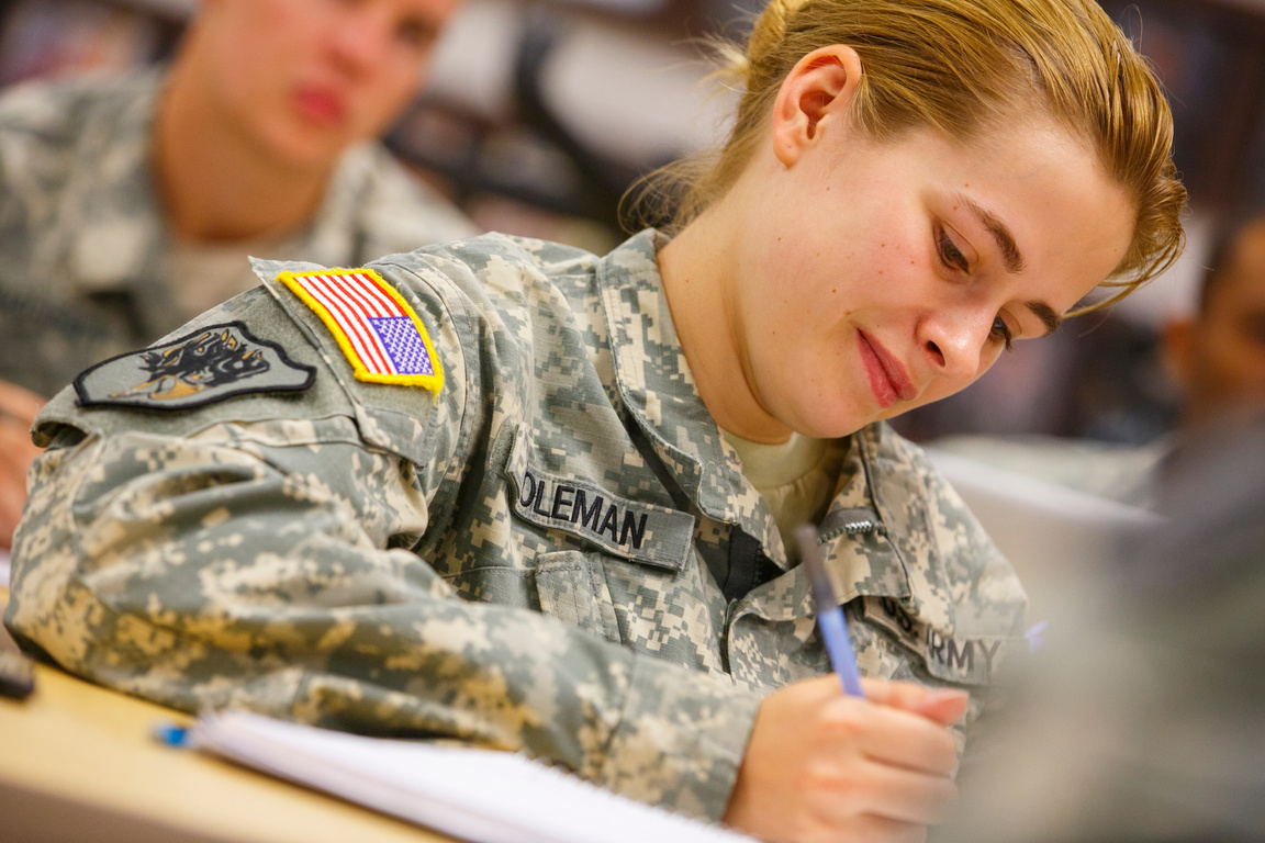 a student in army fatigues is writing on a piece of paper