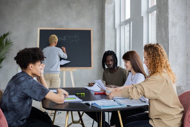 a group of students sitting at a table in front of a blackboard