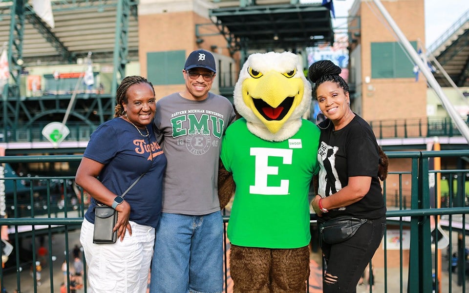 three people pose with Swoop at a baseball game