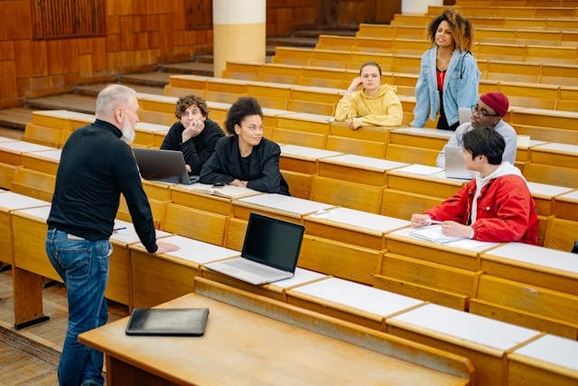 A few people sit in a lecture hall and speak to one another