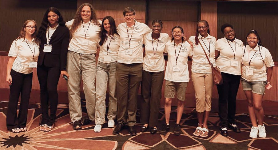 A group photo of the McNair scholars posing in white polos inside an event hall