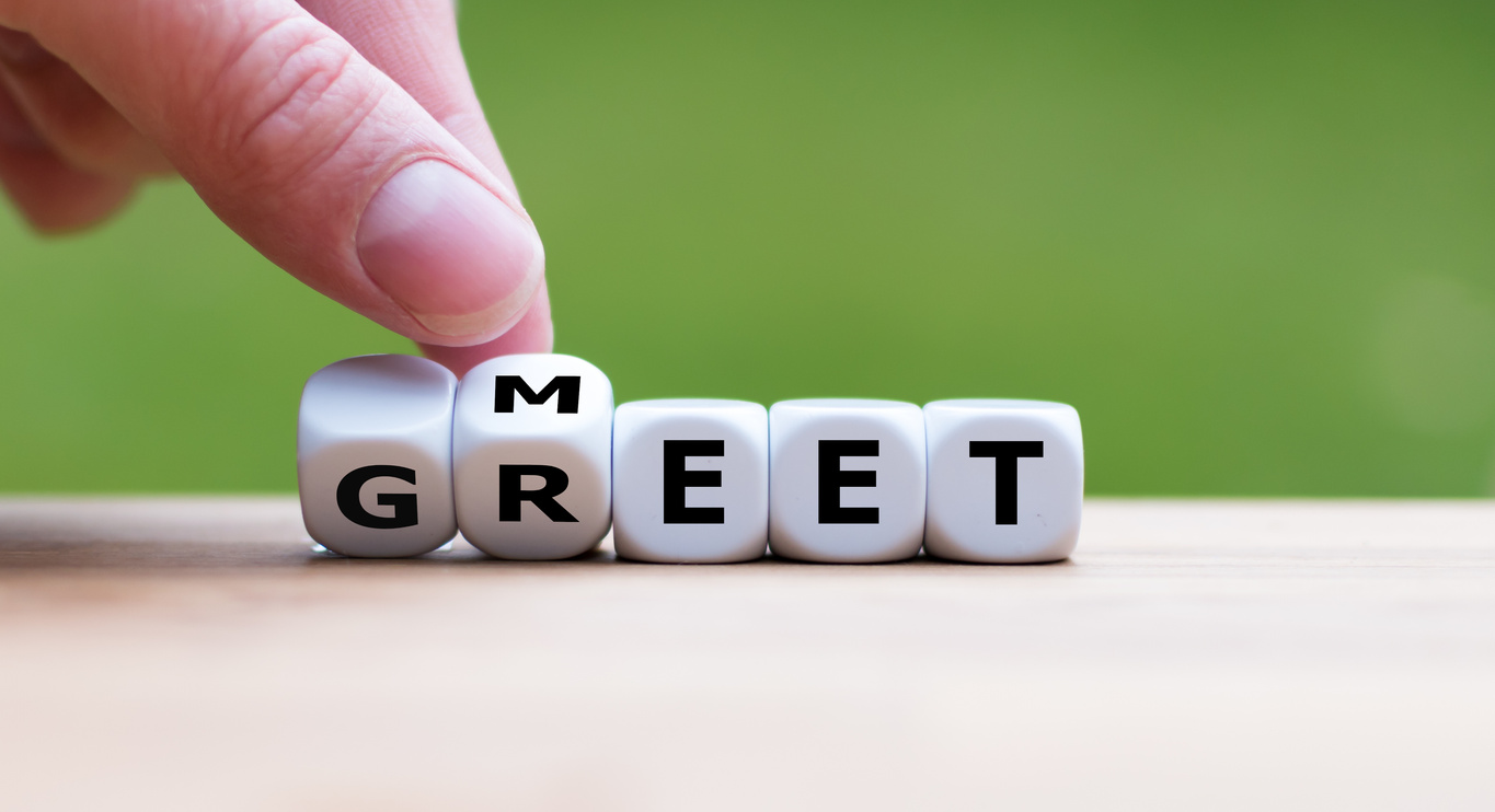 Hand is turning a dice and changes the word "meet" to "greet".