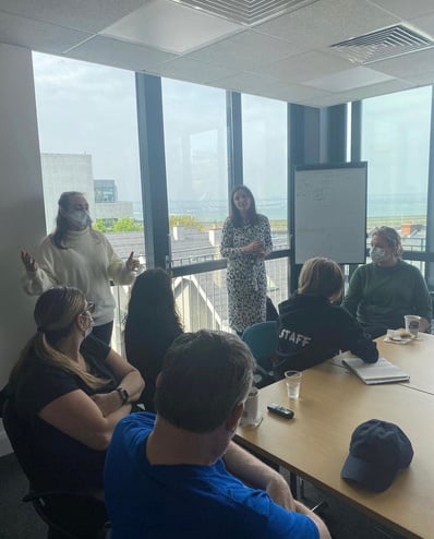 Students speak with facilitators in a conference room with windows showing a view of a city. 