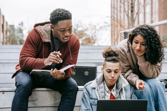 three people sitting on steps looking at a laptop