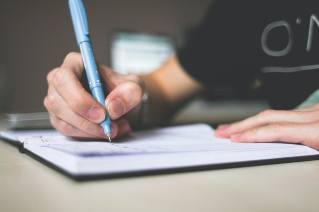 a hand writing with a pen on a notebook