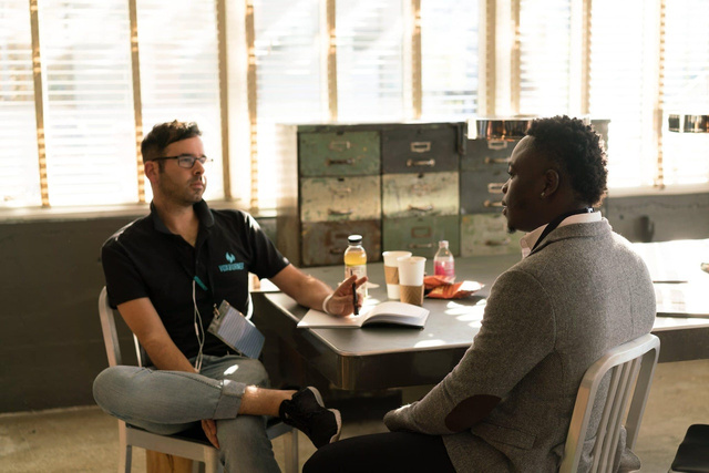 two men sitting at a table talking to each other