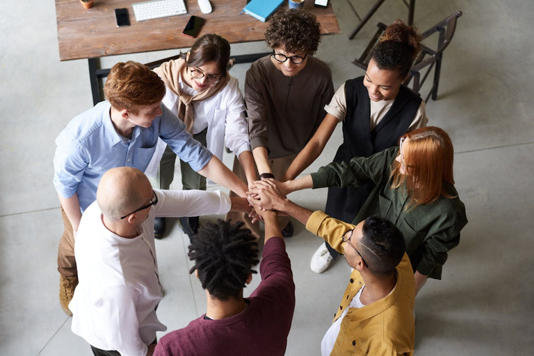 A circle of people put their hands in the center of the circle together